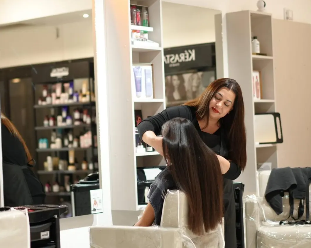 A stylist cutting a client's long hair in front of shelves of Kérastase products